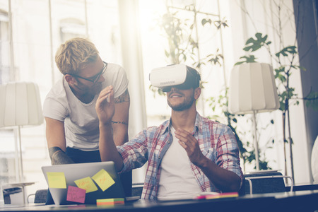 Entrepreneurs testing virtual reality technology with colleague in office.