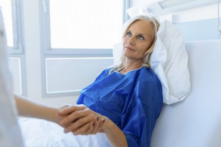 Doctor holding patient's hand in hospital room