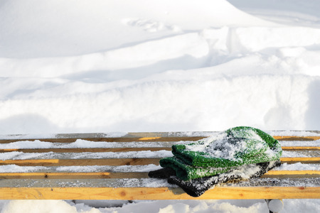 mittens on snow-covered wooden bench on a snowy backgroundの写真素材
