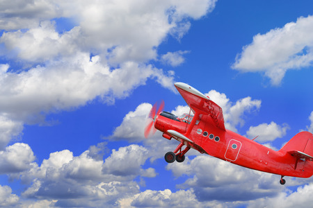 Red airplane biplane with piston engine flies and makes turn in a cloudy sky の写真素材