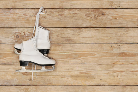 Women's white ice skates hanging on laces on a wooden wallの写真素材