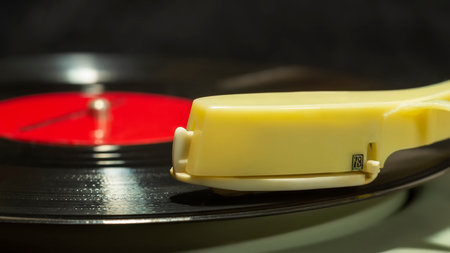 Close up side view of old vinyl record spinning on old turntable player with yellow tonearm on dark blurred backgroundの写真素材