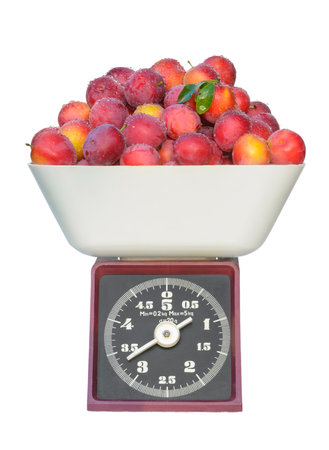 Old mechanical dial scales with fresh juicy plums covered with drops of dew. Isolated on white backgroundの写真素材