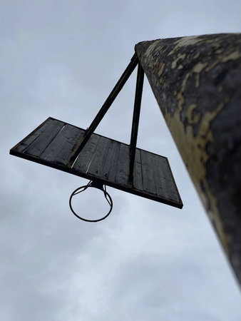 Old wooden basketball hoop hanging on a pole against a cloudy sky.の写真素材
