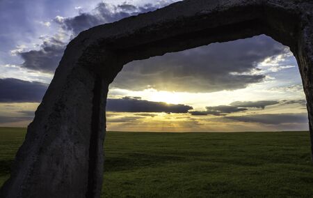 concrete structure stands in the middle of a green meadow at sunriseの写真素材