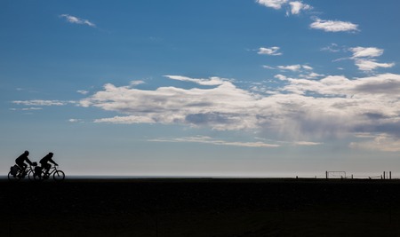 Cyclists silhouette against blue sky and cloudsの写真素材