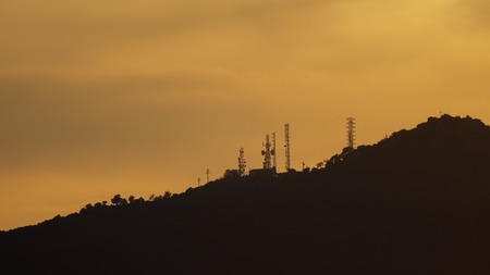 Long shot of sunset over mountains profile with communication towers, orange sky