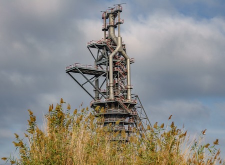 Old blast furnace behind bush and cloudy skyの写真素材