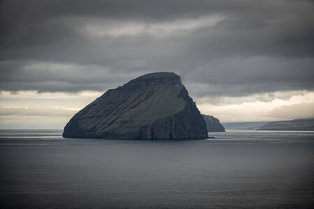 Islet under cloudy sky in Faroe Islandsの写真素材