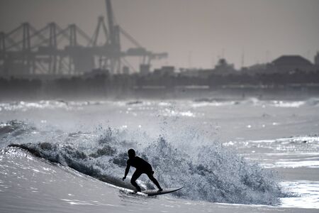 Surfing the waves with cranes in the backgroundの写真素材
