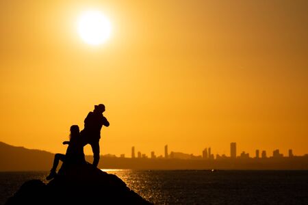 Couple taking social photos at sunset over city skylineの写真素材
