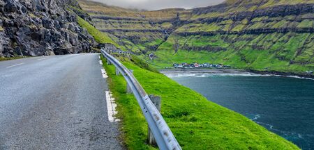 Road to Tjornuvik village with colorful houses surrounded by green mountains in bayの写真素材
