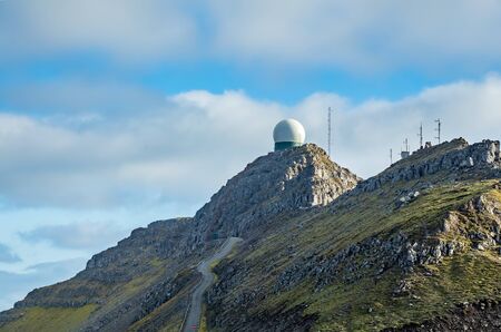 Radar on top of the mountain peak with road ascending and cloudy skyの写真素材