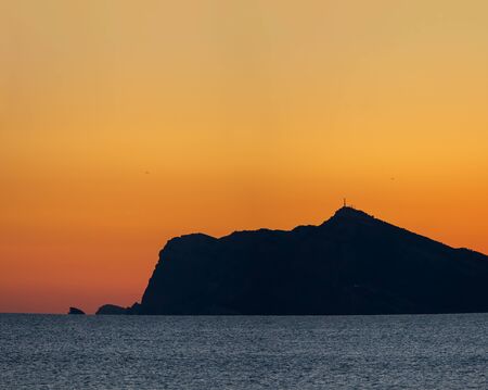 Profile view of huge mountain with antenna near ocean at sunset with orange sky and text spaceの写真素材