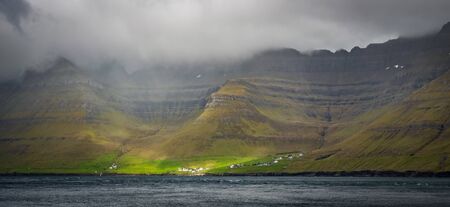 Kunoy, a village in Faroe Islands fjord under steep cliffsの写真素材