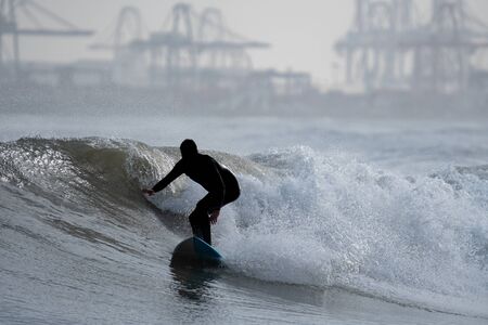 Surfer silhouette surfing the waves near commercial dockの写真素材