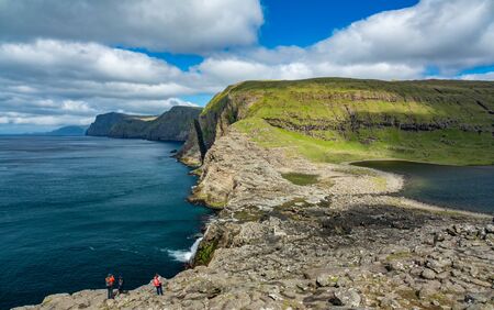 Unrecognizable tourists taking photos to the steep coast in Faroe Islandsの写真素材