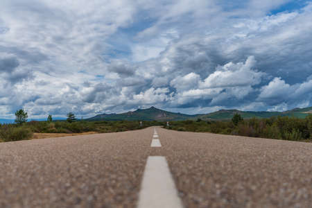 Straight road to mouintain peak under stormy cloudsの写真素材