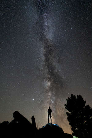 Rear view of 1 person silhouette at night over rocks with milky way