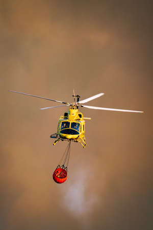 Fire fighter helicopter against dark smoke with water tank