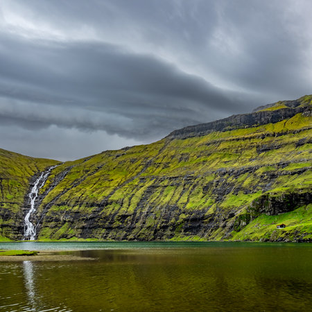 Waterfall and lake under dark stormy cloudsの写真素材