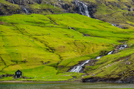 Waterfall, lake and house under the hillの写真素材