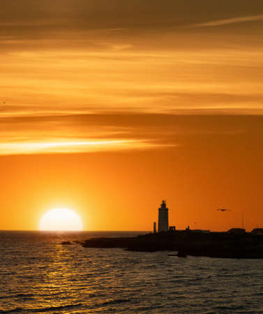 Lighthouse at sunset with sun over the oceの写真素材