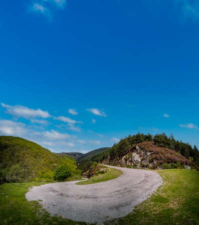 Steep high slope u-shape mountain road under blue skyの写真素材