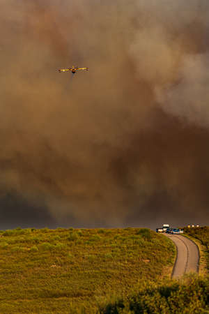 Spectacular hydroplane dropping water over huge fire smokeの写真素材