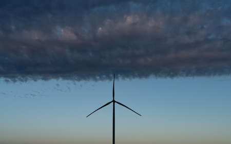 Modern windmill turbine silhouette under the cloudsの写真素材