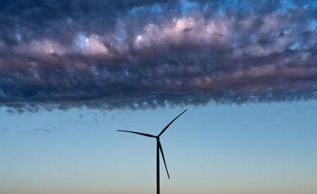 Modern windmill turbine silhouette under dark clouds at sunsetの写真素材