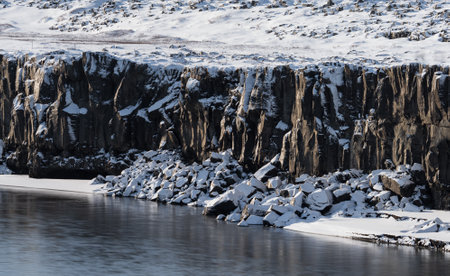 Boulder cubes under the cliffs with snow and riverの写真素材
