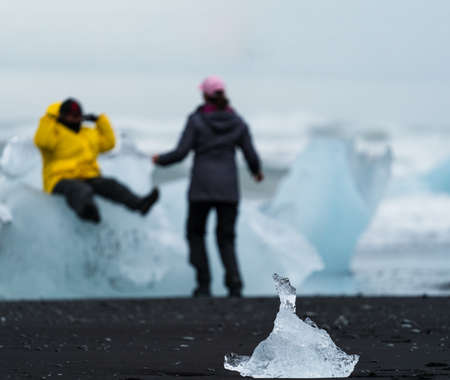 Small block of ice and unrecognizable tourists enjoy icebergsの写真素材