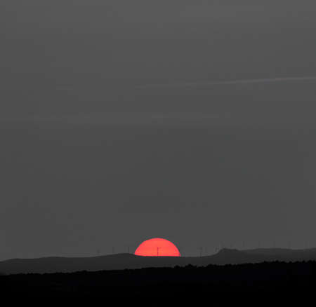 Huge orange half sun at sunset with windmillsの写真素材