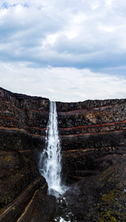 Hengifoss waterfall with deep red layers under cloudy skyの写真素材