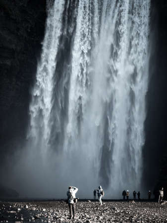 Skogafoss waterfall with tourists taking photos under the streamの写真素材