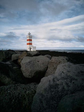 Lighthouse with red stripes wide angle over the black rocksの写真素材