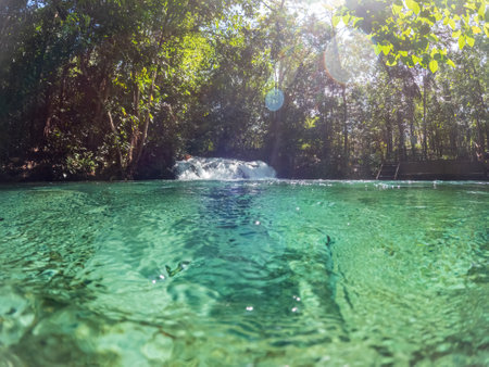 Crystal-clear emerald green waters with waterfall and sunny reflectionsの写真素材
