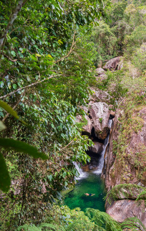 Crystal clear waterhole under colorful jungle waterfalls, with an unrecognizable swimmerの写真素材