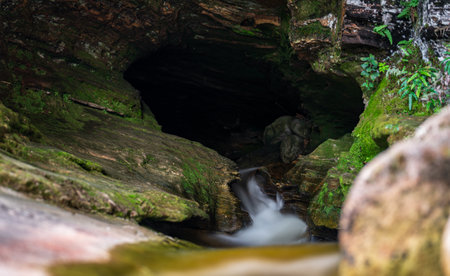 Dark Cave with Silky Waterfall Embracing the Sunlight, Surrounded by Natureの写真素材