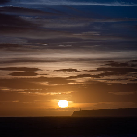 Lighthouse Silhouette on Cliff at Dusk with Calm Sea Backgroundの写真素材