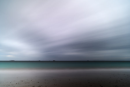 Dramatic Long Exposure of Beach, Sea, and Storm Clouds at Duskの写真素材