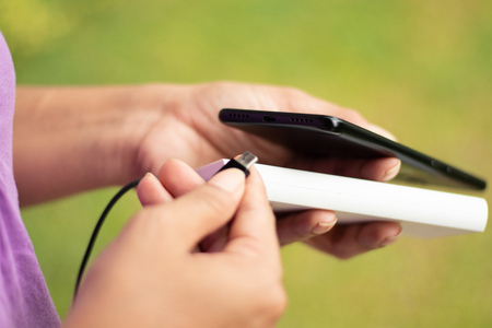 girl hold the phone outside with power bank, green grass