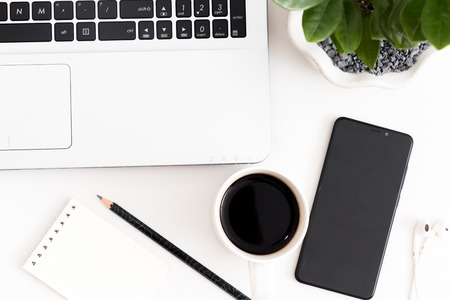 White office desk with laptop, coffee, mobile phone, notebook with pen. Top view with copy space, flat layの写真素材