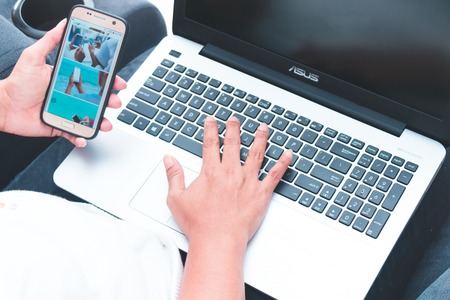 woman holding smart phone and with laptop at office in morning lightのeditorial素材