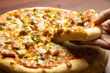 Pan Pizza slice take from hand side view with dark brown woodの写真素材