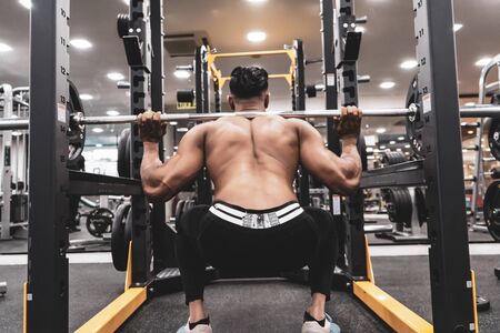 Man at the gym. Execute exercise squatting with weight, in gymの写真素材