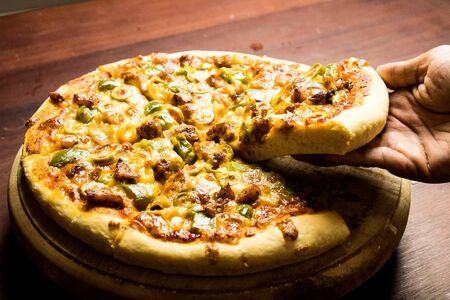 Pan Pizza slice take from hand side view with dark brown woodの写真素材