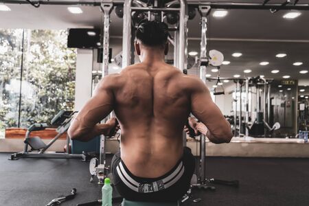 Athlete makes low cable pulley row seated in gym. Close back view
