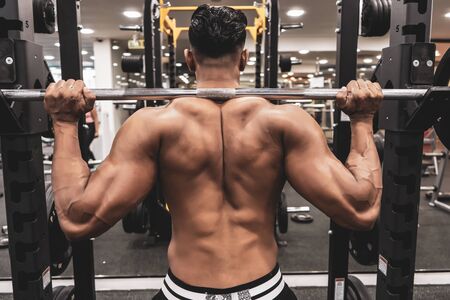 Man at the gym. Execute exercise squatting with weight, in gym